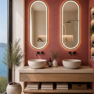 Puede incluir: Un mueble de ba&ntilde;o con dos lavabos redondos sobre una encimera de madera clara, con dos espejos ovalados retroiluminados suspendidos del techo. La pared es de color terracota, con grifos negros montados en la pared y estantes abiertos.