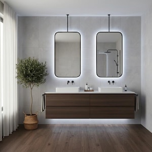 Pode incluir: Uma casa de banho moderna com dois espelhos retangulares com molduras pretas e iluminação integrada. Abaixo, duas pias brancas e uma vaidade de madeira escura. Uma oliveira em vaso e uma janela com cortinas transparentes à esquerda.