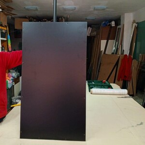 May include: A large, rectangular, dark brown panel suspended from the ceiling by a black pole. The panel is mounted in a workshop setting, with various tools and materials visible in the background.