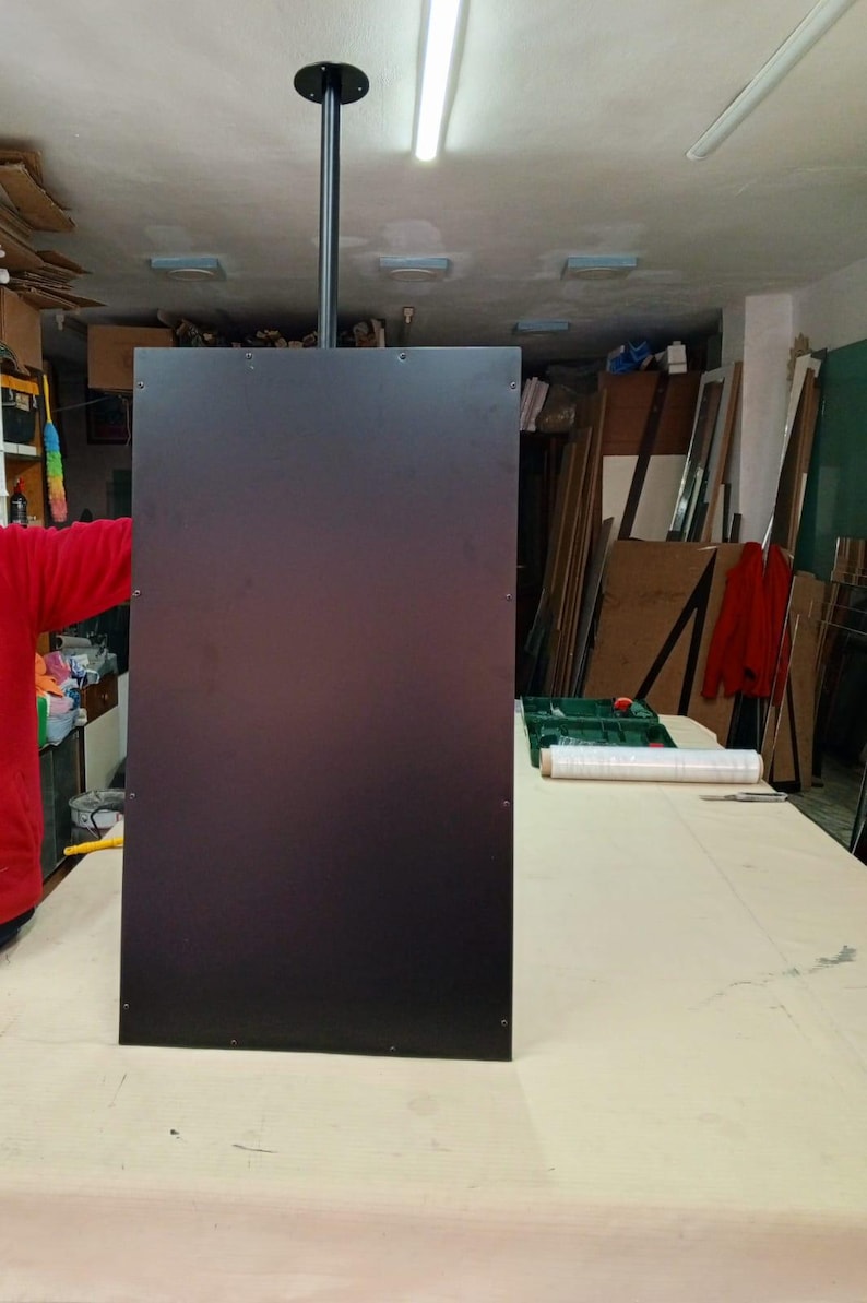 May include: A large, rectangular, dark brown panel suspended from the ceiling by a black pole. The panel is mounted in a workshop setting, with various tools and materials visible in the background.