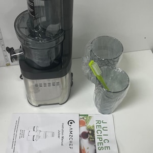 May include: A black and silver AMZCHEF juicer with a clear container and a silver lid. Included are two clear plastic cups, a green and white cleaning brush, and a recipe book. The instruction manual is also visible.