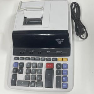 May include: A white and black Sharp EL-2630P II calculator with a built-in printer. The calculator has a full numeric keypad with function keys and a black power cord.