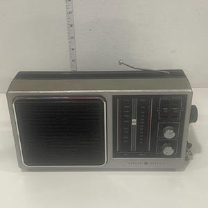 May include: A vintage General Electric AM/FM radio in silver and black. It has a speaker grill, tuning dial, and frequency display. The radio is approximately 30 cm long.