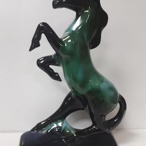May include: A ceramic horse figurine in a rearing pose. The horse is glazed in shades of green and black.