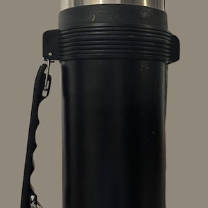 May include: A black and silver thermos with a carrying handle. The thermos has the word "THERMOS" printed on the side.