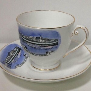 May include: A white teacup and saucer with a blue and white illustration of a ferry boat. The teacup has a gold rim and the saucer has a gold trim. The text "Queen of Sydney" is printed on the teacup.