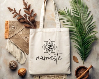 May include: A white tote bag with a fringed bottom. The bag has a black Om symbol inside a mandala design and the word "namaste" printed on it.