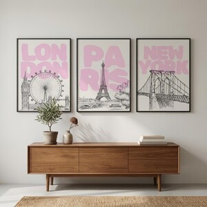 May include: Three framed art prints featuring iconic city landmarks. The prints display the London Eye, Eiffel Tower, and Brooklyn Bridge, each with a pink city name overlay. The artwork is in black and white, with a neutral background.