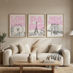 May include: Three framed art prints featuring iconic city landmarks. The prints display the London Eye, Eiffel Tower, and Brooklyn Bridge, each with a pink city name overlay. The artwork is in black and white with a light beige background.