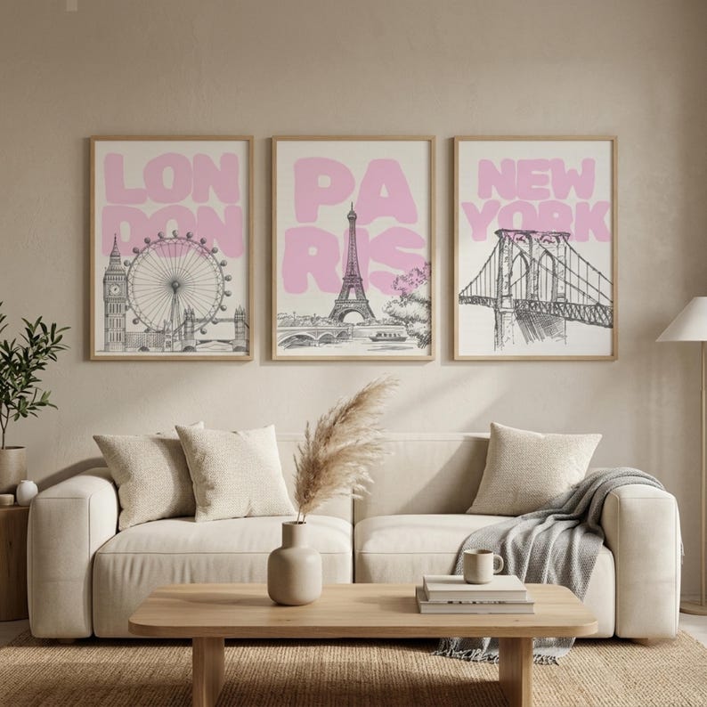 May include: Three framed art prints featuring iconic city landmarks. The prints display the London Eye, Eiffel Tower, and Brooklyn Bridge, each with a pink city name overlay. The artwork is in black and white with a light beige background.