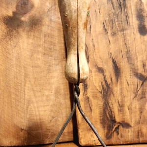 Puede incluir: Un machacador de patatas vintage con mango de madera y cabeza de machacado de alambre retorcido. El machacador es de metal y madera y tiene un aspecto rústico.