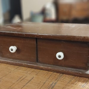 May include: A small wooden box with two drawers and white knobs. The box is brown and has a distressed finish.