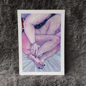 Peut inclure: Une impression d'art rectangulaire présentant un dessin au crayon de couleur de deux silhouettes enlacées. Les personnages ont des tons de peau rosés et portent des menottes argentées aux poignets et aux chevilles sur un fond blanc.