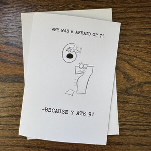 May include: A white greeting card with the text "WHY WAS 6 AFRAID OF 7?" and the answer "-BECAUSE 7 ATE 9!" in black ink. The card features cartoon drawings of the numbers 6 and 7.