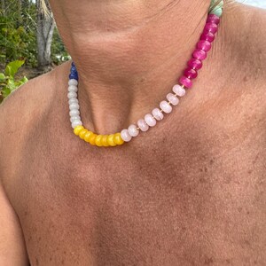 May include: A colorful beaded necklace with a variety of gemstone beads. The necklace features a gradient of colors, including blue, white, yellow, pink, and magenta. The beads are strung together, creating a vibrant and eye-catching accessory.