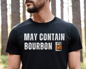 May include: A black t-shirt with the text "May Contain Bourbon" in white distressed lettering. A glass of amber liquid with ice cubes is to the right of the text.