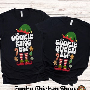 May include: Two black t-shirts with a Christmas elf design. The text on the shirts reads "The Cookie King Elf" and "The Cookie Queen Elf".