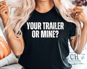 May include: A black t-shirt with white text that reads "YOUR TRAILER OR MINE?" The shirt is being worn by a person with blonde hair and blue jeans.