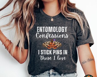 May include: Dark gray t-shirt with the text "ENTOMOLOGY Confessions I STICK PINS IN Those I love" and a graphic of a butterfly with pins. The shirt is a crew neck and is made of a soft material.