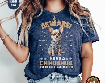 May include: A heather navy blue t-shirt with a chihuahua wearing a denim jacket. The text on the shirt reads "BEWARE! I HAVE A CHIHUAHUA AND I'M NOT AFRAID TO USE IT."
