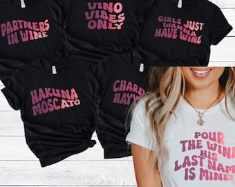 May include: Set of six black t-shirts with pink text. The shirts feature various wine-themed phrases, including "Partners in Wine", "Vino Vibes Only", "Girls Just Wanna Have Wine", "Hakuna Moscato", "Chardonnay", and "Pour the Wine His Last Name is Mine".