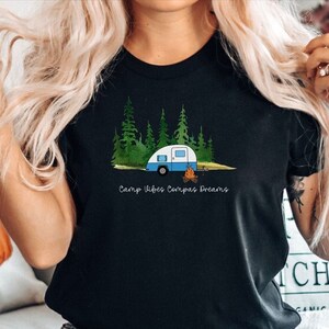 May include: Black t-shirt with a graphic of a blue camper in a forest with a campfire. The text "Camp Vibes Compass Dreams" is printed below the graphic.
