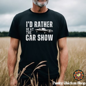 Peut inclure: Un t-shirt noir avec un motif blanc qui dit "J'aimerais mieux &ecirc;tre au salon de l'auto". Le motif comprend &eacute;galement une voiture de sport noire.