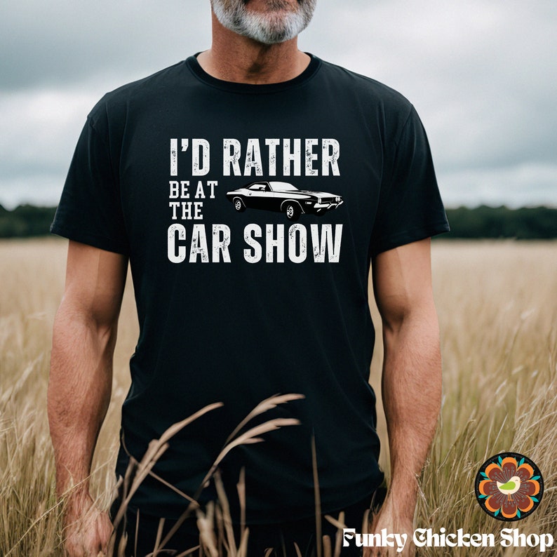 Peut inclure: Un t-shirt noir avec un motif blanc qui dit "J'aimerais mieux &ecirc;tre au salon de l'auto". Le motif comprend &eacute;galement une voiture de sport noire.