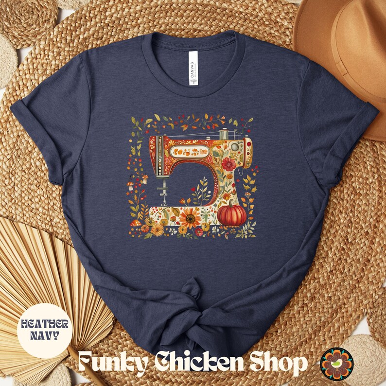 May include: Heather navy blue t-shirt featuring a colorful illustration of a vintage sewing machine adorned with flowers and a pumpkin. The shirt has the text "Funky Chicken Shop" at the bottom.