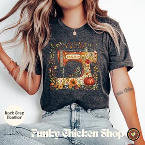 May include: Dark grey heather t-shirt featuring a colorful sewing machine design. The sewing machine is decorated with floral and pumpkin motifs. The shirt also has the text "Funky Chicken Shop".