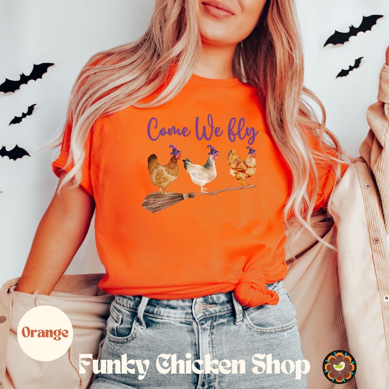 May include: Orange t-shirt with the text "Come We Fly" and a graphic of three chickens wearing witch hats and riding a broomstick.