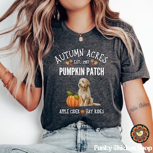 May include: A gray t-shirt with the text "Autumn Acres Est. 1987 Pumpkin Patch Apple Cider Hay Rides" and a cartoon image of a golden doodle dog sitting next to a pumpkin.