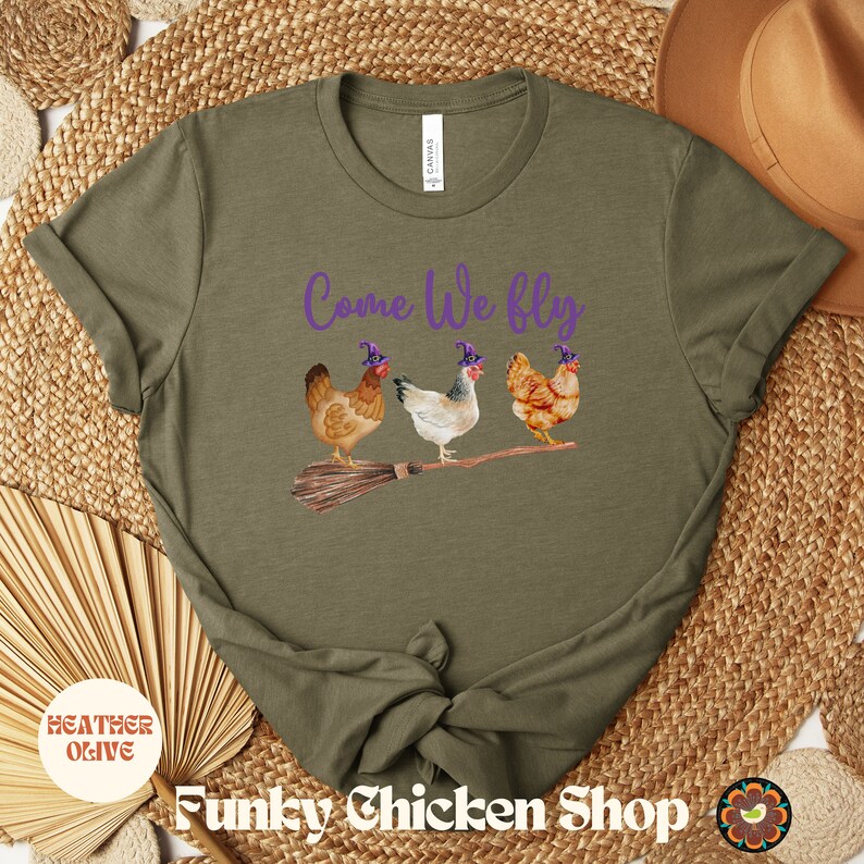May include: A green t-shirt with the text "Come We Fly" in purple lettering. Three chickens wearing witch hats are flying on a broomstick.