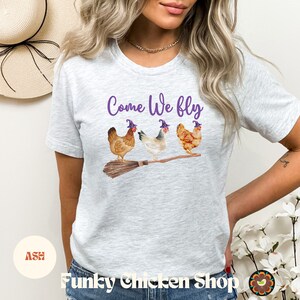 May include: A grey t-shirt with the text "Come We Fly" and a graphic of three chickens wearing witch hats and riding a broomstick.