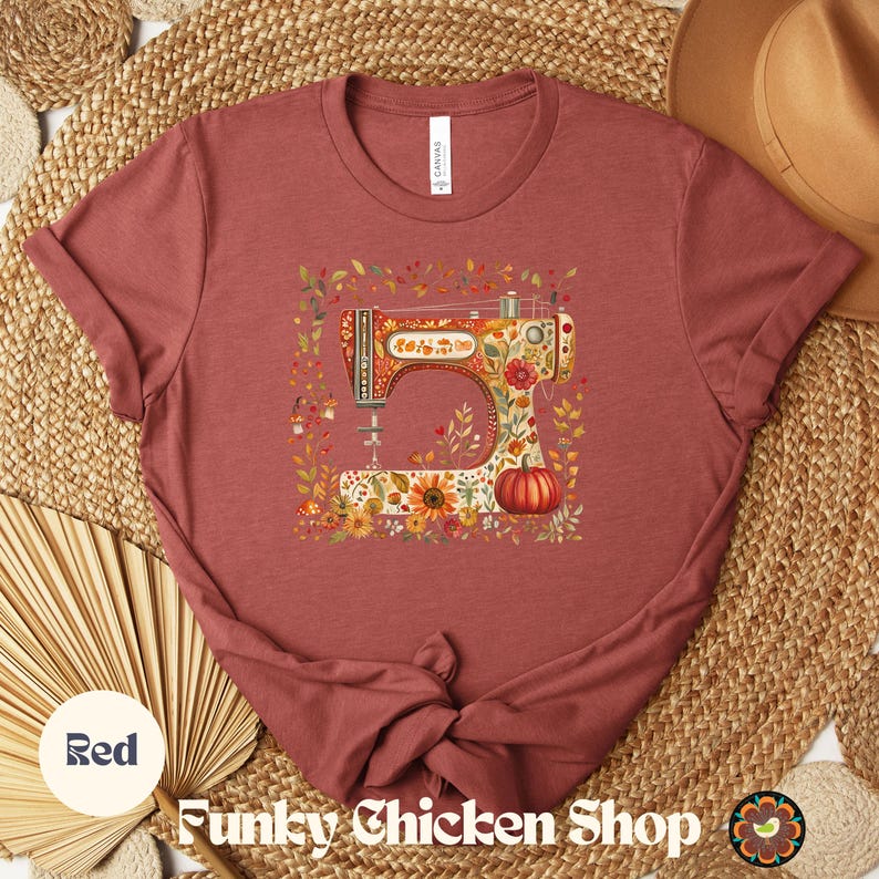 May include: Red t-shirt featuring a colorful illustration of a vintage sewing machine decorated with flowers and a pumpkin. The text "Funky Chicken Shop" is at the bottom. The shirt is made of soft material.