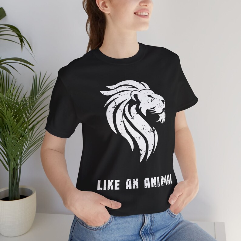 K&ouml;nnte beinhalten: Schwarzes T-Shirt mit einem wei&szlig;en L&ouml;wen-Motiv und dem Aufdruck "LIKE AN ANIMAL" auf der Vorderseite.