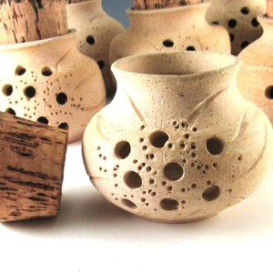 May include: Handmade ceramic jars with cork stoppers. The jars are a light beige color with a textured surface and decorative holes. The cork stoppers are a dark brown color. The jars have a unique, rustic design.
