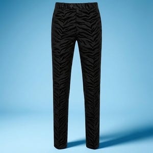 Puede incluir: Pantalones negros con un patrón de rayas de cebra tonal y aterciopelado. Estos pantalones incluyen una cintura con trabillas para cinturón, un cierre de botón centrado en la parte superior y un corte recto hasta el dobladillo.