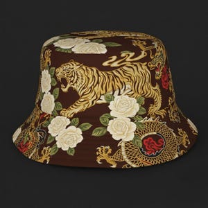 May include: Brown bucket hat with a repeating pattern of a tiger, white roses, and a dragon. The tiger is gold and black, the roses are white, and the dragon is gold and red. The hat is a stylish accessory.
