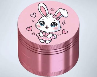 May include: A pink metal grinder with a cartoon bunny illustration on top. The bunny has big blue eyes, a pink bow, and a pink dress. Pink hearts surround the bunny. The grinder has a textured, ridged design.