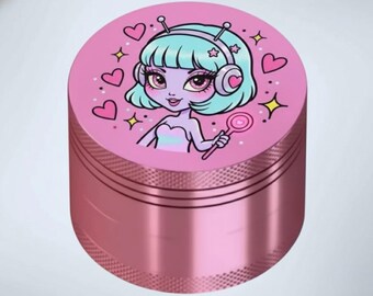 May include: A pink metal grinder with a cartoon alien girl design. The top features a light blue-haired alien with pink hearts, stars, and a lollipop. The grinder has a textured, metallic finish.