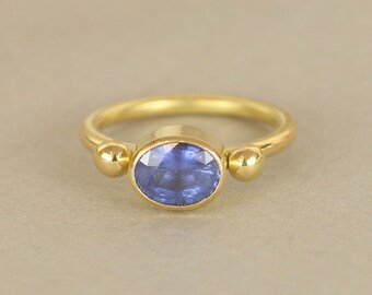 May include: A gold ring featuring a blue oval sapphire gemstone, flanked by two smaller gold beads.