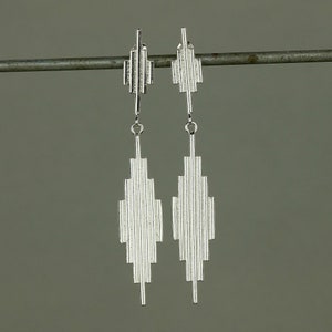 May include: A pair of silver dangle earrings with a geometric design. The earrings are made of thin, vertical lines that create a diamond shape.