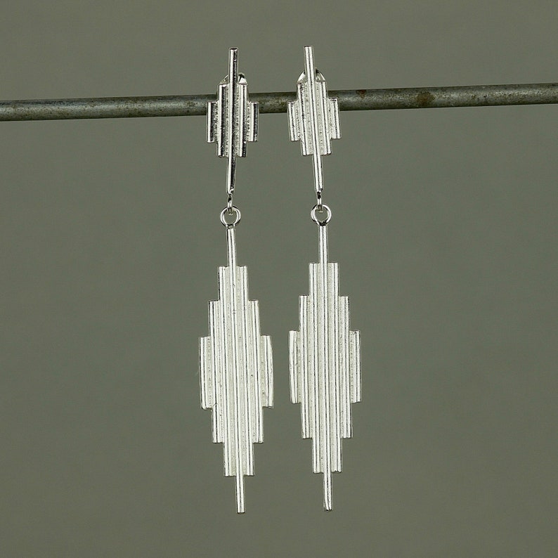 May include: A pair of silver dangle earrings with a geometric design. The earrings are made of thin, vertical lines that create a diamond shape.