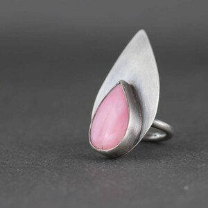 May include: A silver ring with a pink teardrop-shaped gemstone set in a leaf-shaped design.