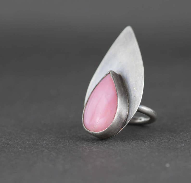 May include: A silver ring with a pink teardrop-shaped gemstone set in a leaf-shaped design.