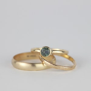 Puede incluir: Tres alianzas de oro, una con una piedra preciosa verde. Las alianzas est&aacute;n apiladas una encima de la otra.