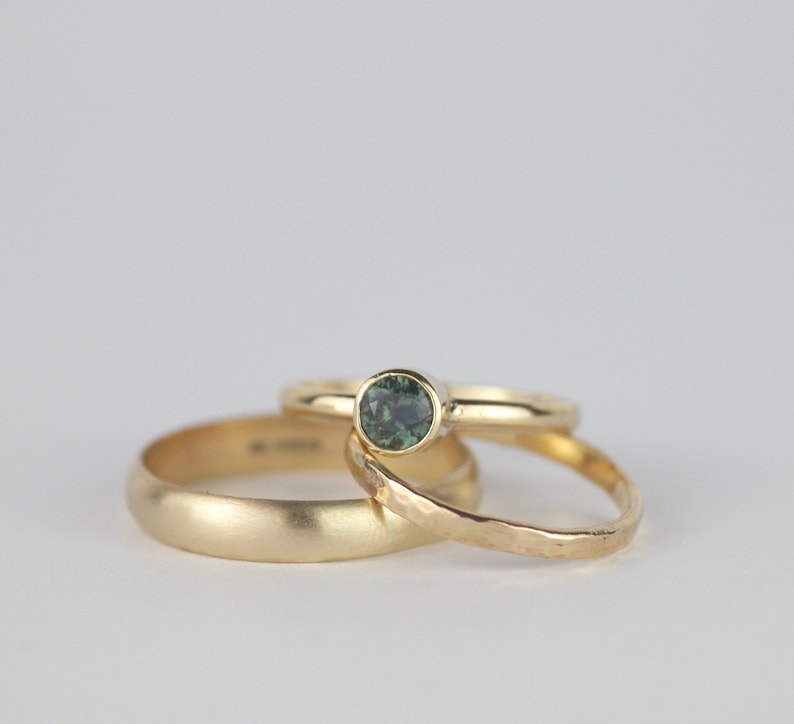 Puede incluir: Tres alianzas de oro, una con una piedra preciosa verde. Las alianzas est&aacute;n apiladas una encima de la otra.