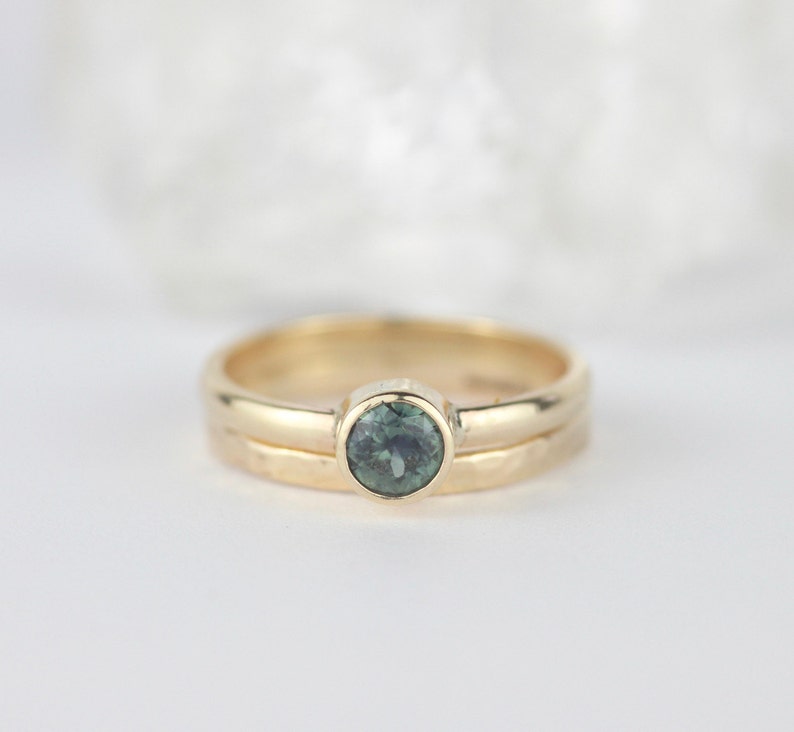 K&ouml;nnte beinhalten: Ein Goldring mit einem gr&uuml;nen Edelstein, der in einer Zargenfassung gefasst ist. Der Ring ist schlicht gehalten und hat eine geh&auml;mmerte Textur.