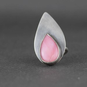 May include: A silver ring with a teardrop-shaped pink opal gemstone set in a silver bezel.
